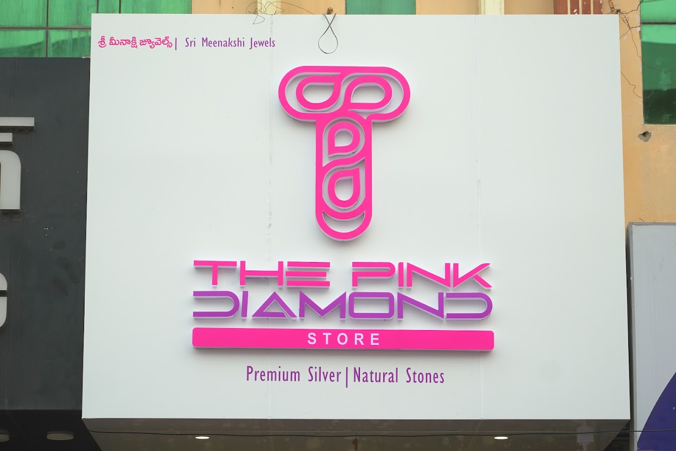 Storefront photo of The Pink Diamond Store, Guntur with pink logo in the foreground and White Background