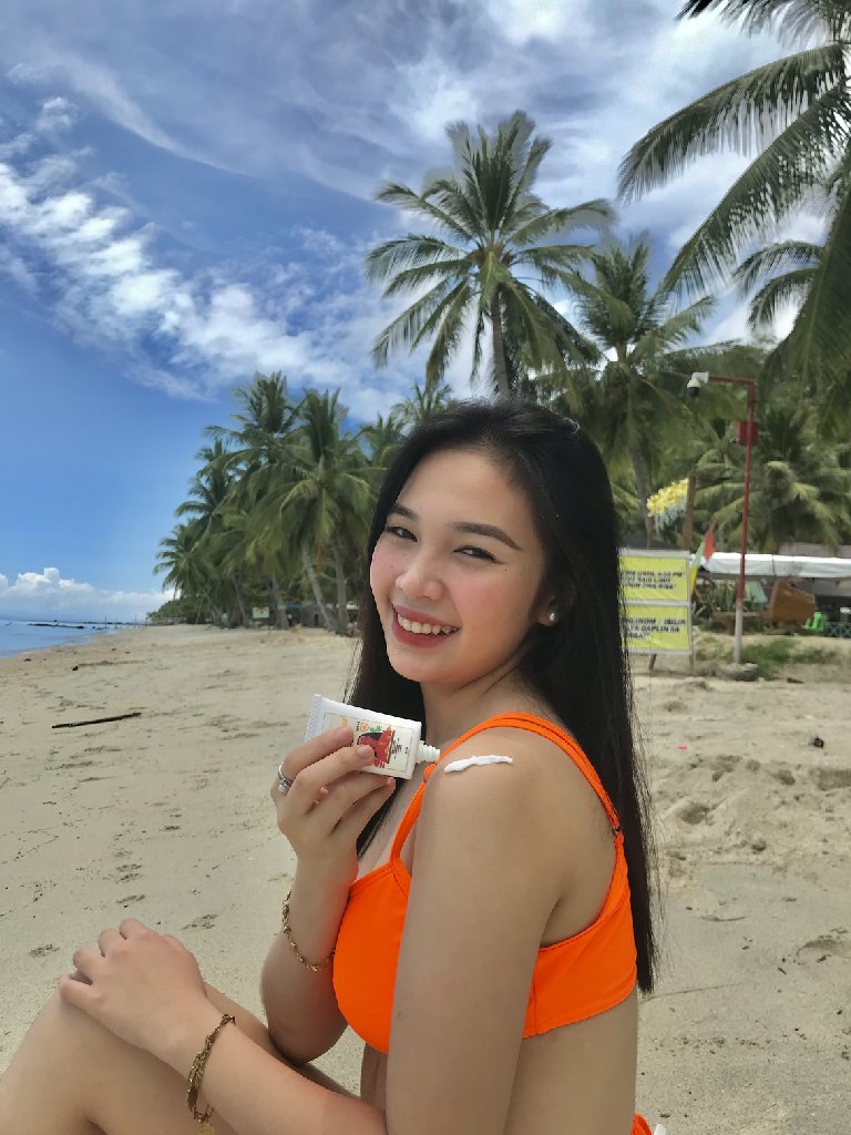 A beautiful model applies Beautifilipina Sun Dazed Sunscreen SPF 45 onto her shoulder on a beach in the Philippines.